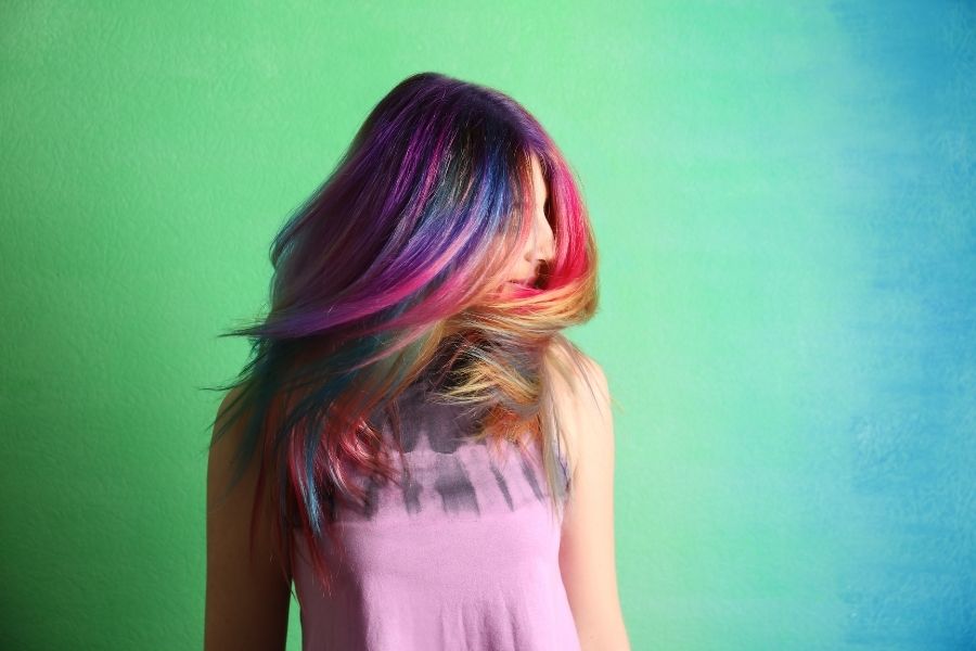 Woman with vibrant rainbow hair color showing latest hairstyles tendance against colorful backdrop