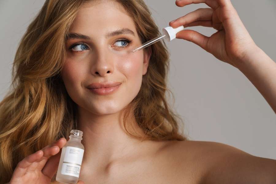 A smiling woman applies peptide serum with a dropper to her skin.