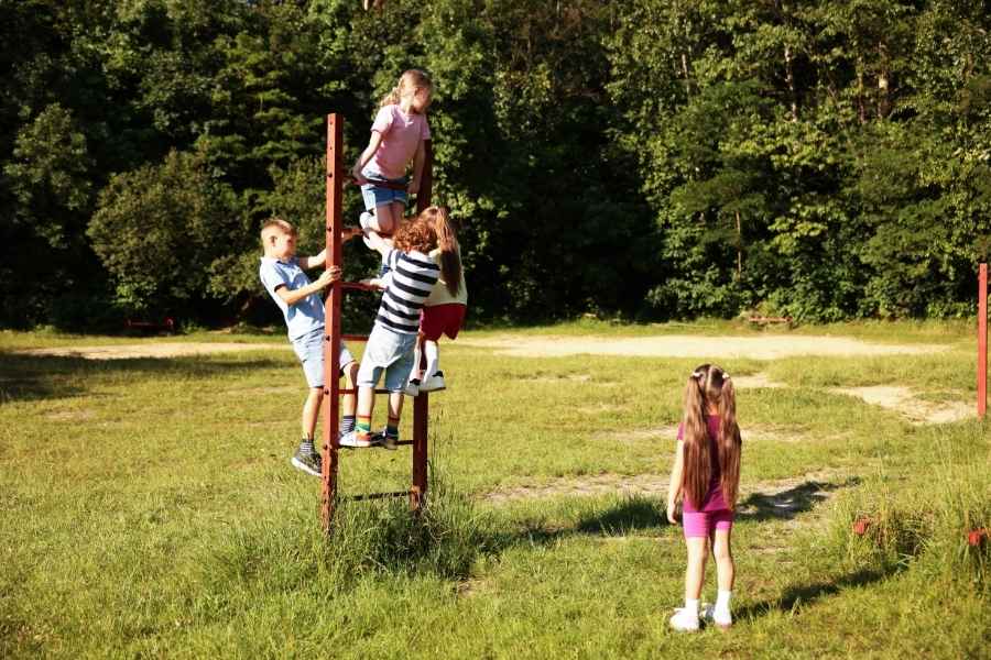 Three boys laughing and running across a green lawn toward a colorful tent, enjoying outdoor activities on a sunny day.