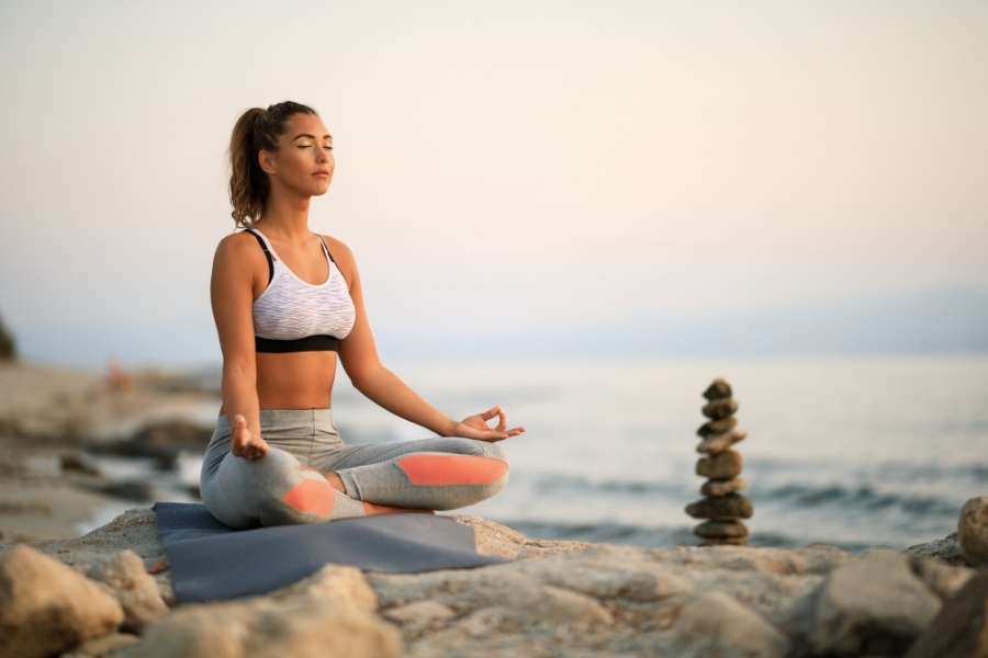 A woman meditating on a beach rock during calm mindfulness exercises.